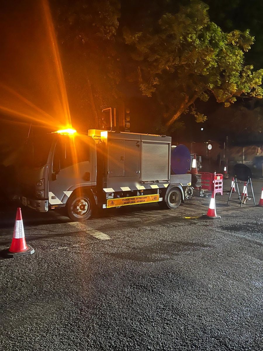 Drain jetting truck parked on a street at night with amber beacon on and the work area coned off